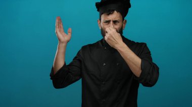 Siyah üniformalı İspanyol aşçı burnu kötü kokuya tepki veriyor. Mutfak ortamındaki iğrenme ifadelerini vurguluyor..