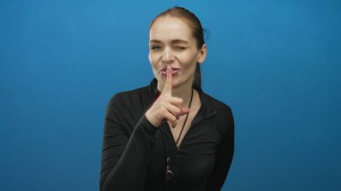 Siyah kabzalı genç beyaz koç parlak mavi stüdyodaki parlak mavi ipli kameraya işaret ediyor..