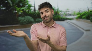Erkek, sıradan bir polo tişört giyen ve geniş bir şekilde gülümseyen, Line Street 'te açık elleri olan jestler yapar..