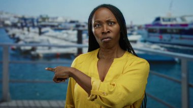 Sarı gömlekli kadın deniz kıyısında görünür botlarla dikiliyor..