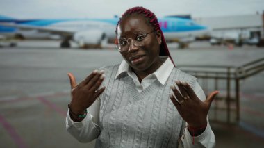 Havaalanı terminalinde arka planda uçakla gülümseyen bir kadın seyahat ve seyahat önerisi sunuyor. İlişkili içerik için gündelik bir ortamda neşeli bir ifade sergiliyor.