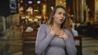 Arka planda bulanık sıraları ve vitray pencereleri olan güzel aydınlatılmış bir kilisede duygularını ve ruhaniliğini ifade eden bir kadın..