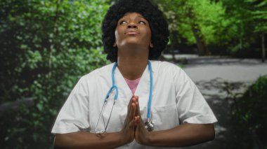 Steteskoplu kadın doktor parkta yeşil ağaçların altında dua ederken el ele tutuşuyor..