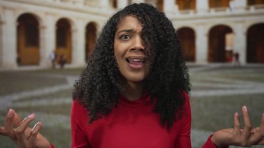 Afrika kökenli Amerikalı bir kadın eski kasabadaki tarihi bir bina avlusunda kıvırcık saçlarına dokunuyor ve avuçlarıyla işaret ediyor..