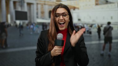 Vatikan St. Peter Meydanı 'nda güvenli bir şekilde gülümseyen kadın muhabir arka planda kalabalıkla açık hava haberlerini kaydediyor..