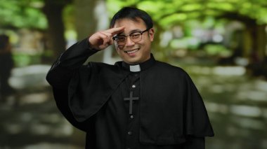 Güneşli parkta yeşil ağaçlarla gülümseyen siyah cüppeli Asyalı rahip..