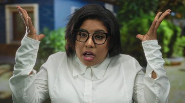 Gözlüklü ve beyaz tişörtlü bir kadın yeşil ağaçlı bir caddede sürpriz yapıyor..