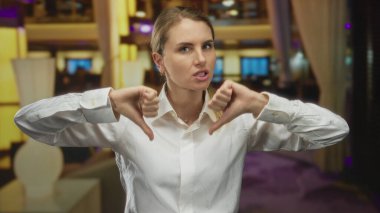 Zarif bir otel lobisinde hoşnutsuzluğunu dile getiren bir kadın sofistike iç dekorasyon ve hafif ışıklandırma arasında dramatik bir jest yakalıyor..