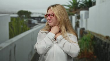 Şehirdeki caddede gözlüklü ve beyaz gömlekli, sıkıntılı bir ifadeyle boğulan, yemyeşil ve uzak kentsel zemin tarafından vurgulanan bir kadın..