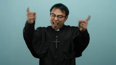 Rahip gibi giyinmiş mutlu bir adam gülümsüyor ve mavi bir arka plana işaret ediyor.