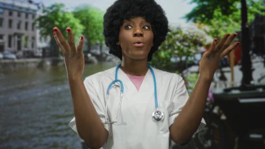 Beyaz önlük ve steteskop giyen kadın doktor, binanın önündeki sokakta avuç içleriyle omuz silkiyor..
