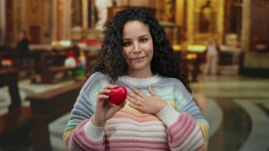 Kilisenin içinde kalp sembolü taşıyan kadın, dingin bir atmosferde sıcaklığı ve bağlılığı simgeleyen, İspanyol kültüründe yakalanmış ruhani nezaketi ve bağlantıyı simgeler..