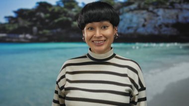 Deniz kenarına gülümseyen, çizgili bir kazak giyen, güneşli gökyüzünün altında neşeli açık hava anları yakalayan bir kadın..