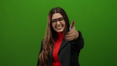 Gülümseyen ve elini uzatan bir kadın, canlı yeşil arka plana karşı resmi giyinmiş, yaklaşımını ve güvenini ifade eden, kurumsal ortamlar için ideal..