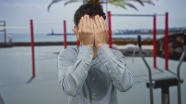 Genç İspanyol adam, jimnastik barlarının girişinde yüzünü iki eliyle kapatıyor..