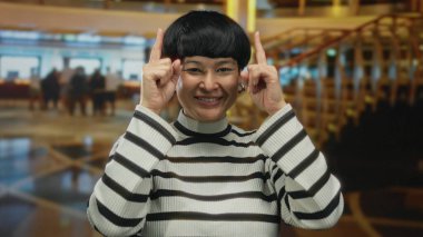 Çizgili süveter giymiş bir kadın otelin içine doğru bakıyor neşeli bir ifade ve modern bir moda sergiliyor..