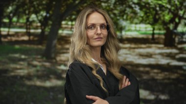 Üniformalı genç sarışın kadın yargıç yeşil bir park ortamında duruyor, otoritenin ve doğanın bir görüntüsünü yakalıyor..