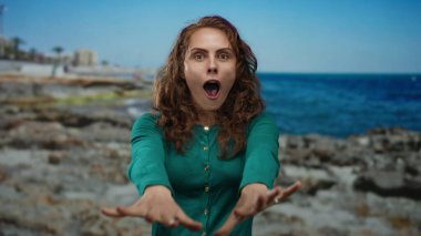 Kayalık bir sahil kenarında, berrak bir gökyüzünün altında canlı bir mavi denizle duygularını ifade eden bir kadın, açık havada genç bir neşe yakalıyor..