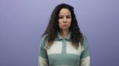 Çizgili kazaklı kıvırcık saçlı kadın, mor duvara karşı üzgün görünüyor. Stüdyoda tek başına melankolik duygularını ifade ediyor. Yalnızlık ve tefekkür hissi uyandırıyor..