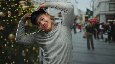 Gri tişörtlü, enerjik bir şekilde gülümseyen genç adam, neşeli şehir sokaklarında bayram kutlamaları için süslenmiş..