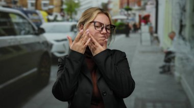 Gözlüklü ve sarı saçlı bir kadın işlek bir caddede açık havada şehir ortamında iletişim ya da duyguyu ifade eder..