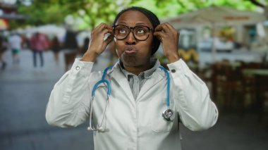 Gözlüklü kadın doktor ve steteskoplu beyaz önlüklü kadın kalabalık bir şehir sokağında duruyor..