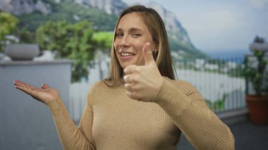 Genç sarışın kadın, balkonda avuç içini işaret ediyor; öneri onayı.