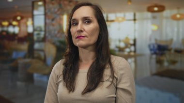 Kapalı bir yerde kendine güveni olan bir kadın hafifçe aydınlatılmış bir ortamda, davet edici ışık ve dekora karışıyor, rahat bir iç mekan görüntüsü yakalıyor..