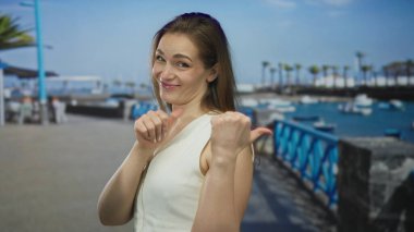 Beyaz kolsuz üst puanları olan kadın mavi korkulukların olduğu güneşli bir sahil geçidinde kendini parmaklıyor..