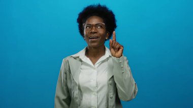 İzole edilmiş mavi arka planda, gözlük takan ve ilham anında beyaz gömlek giyen bir kadın..