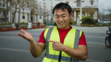 Parlak yelekli genç adam, şehir sokaklarında elleri açık gülümsüyor profesyonel ve dostane bir tavırla kentsel bir çevrede gösteri sunuyor..