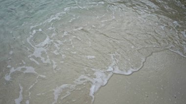 Mallorca 'da kumlu bir sahilde dalgalanan hafif dalgalar berrak mavi su ve yumuşak köpükle sakin bir plaj sahnesi yaratır..