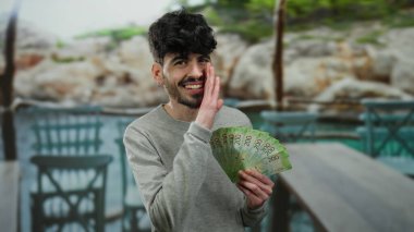 Elinde Rus rublesi tutan bir adam açık terasta restoran dekoruyla fısıldıyor, oyuncu ve yakışıklı görünüyor, elinde para ile sokak atmosferini yakalıyor..