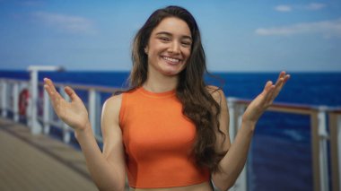 Turuncu mahsullü kadın geniş bir gülümseme ile yolcu güvertesinde mavi gökyüzü altında deniz kenarında ellerini kaldırdı; keyif özgürlüğü macera eğlence.