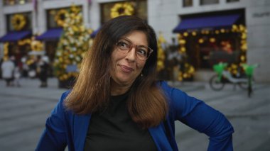 Gözlüklü ve mavi ceketli bir kadın, dükkan dekorasyonlarıyla sokakta dilini dışarı çıkarıyor..