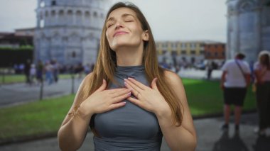 Kafkasyalı genç kadın, nazikçe gülümserken kule binasının ön cephesine karşı narin parmaklarını kalp şeklinde kaldırır..