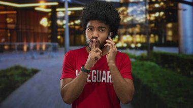 Cankurtaran tişörtlü bir adam gece vakti şehir sokağında akıllı telefon kullanıyor. Bu Amerikan ortamında şehir ışıkları altında sessizlik için işaret veriyor..