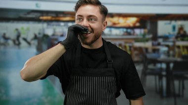 Havalimanı terminalinde önlük ve eldiven giymiş genç, beyaz bir garson arka planı bulanık ve eldivenini düzeltirken gülümsüyor..