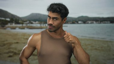 Güneşli sahil kıyısında kumlu sahili ve sakin su arkaplanını izlemek için parmak göze hareket eden bir adam..