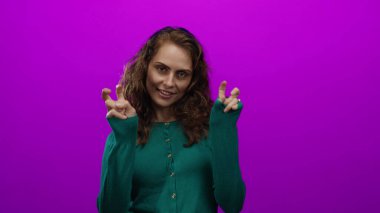 Genç bir kadın neşeli bir şekilde pembe bir arka plana karşı hareketli, kıvırcık saçlarıyla ve günlük tarzıyla duygularını ifade ediyor, tavır sergiliyor ve çevreden soyutlanıyor..