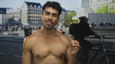 Üstsüz adam şehir meydanında altın güneş ışığı altında granola çubuğu tutuyor..