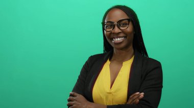 Örgülü ve gözlüklü kendine güvenen bir kadın yeşil arka plana gülümsüyor, zarafet ve profesyonellik sergiliyor.