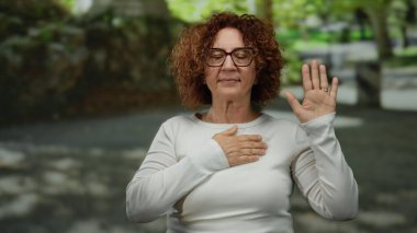 İspanyol kadın, sakin bir park ortamında, gözlük ve beyaz gömlek takarak, yeşil ve taştan yollarla çevrili bir vaadi ya da yemini sembolize ediyor..