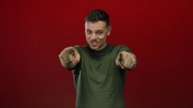 Yeşil gömlekli genç adam kırmızı arkaplanı işaret ediyor. Kendine güveni ve karizması var..