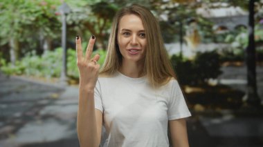 Yapraklı ağaçlar ve patikalarla çevrili yemyeşil bir açık hava parkında neşeli bir şekilde gülümseyen kadın doğada bir neşe ve rahatlama hissi taşıyor..