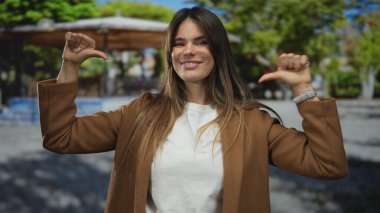 Açık şehir ortamında kendini gösteren başparmaklarıyla gülümseyen bir kadın güneşli bir günde kendine güven ve mutluluk gösteriyor..
