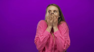 Pembe tişörtlü genç bir kadın, mor arka plana karşı şaşkınlıkla ağzını kapatarak şok ve duygunun samimi bir ifadesiyle görüntülendi..