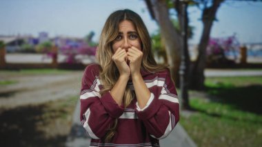 Gölgeli bir parkta tırnaklarını yiyen bir kadın çiçek açan bougainvillea ağaçlarının yanında..