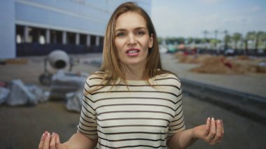 Kadın büzüşmüş dudaklarıyla yüzünü buruşturuyor ve bina önünde elini göğsüne yaklaştırıyor..