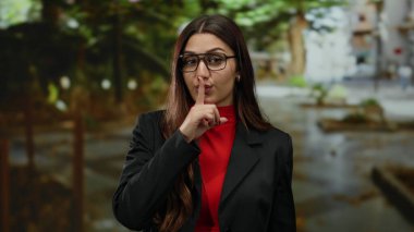 Açık hava parkında gülümseyen yeşil arka planda kırmızı gömlek ve gözlük takan genç İspanyol tarzı kendine güvenen ve zarif bir kadın..